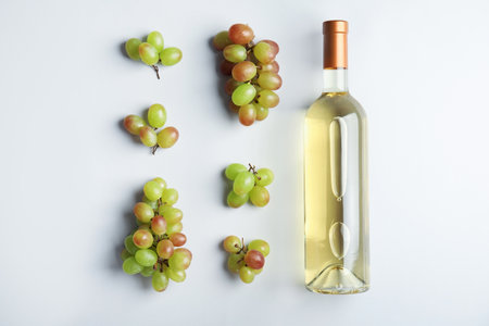 Bottle with white wine and fresh ripe juicy grapes on light background, top viewの写真素材
