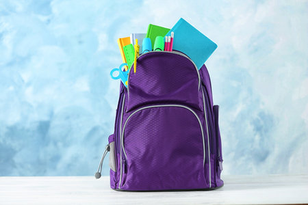 Backpack with school stationery on table against color backgroundの写真素材