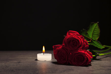Beautiful red roses and candle on table against black background. funeral symbolの写真素材