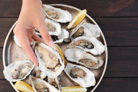 Top view of woman with fresh oyster over plate, focus on handの写真素材
