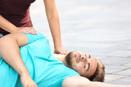 Woman checking pulse of unconscious man outdoorsの写真素材