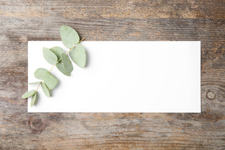 Fresh eucalyptus leaves and blank card with space for design on wooden background, top viewの写真素材