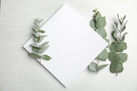 Fresh eucalyptus leaves and blank card with space for design on wooden background, top viewの写真素材