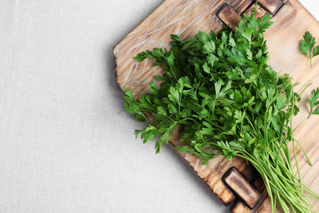 Wooden board with fresh green parsley and space for text on light fabric, top viewの写真素材