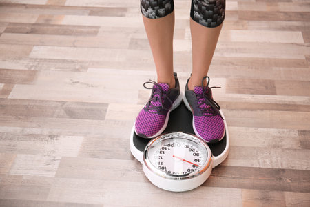 Woman measuring her weight using scales on floorの写真素材