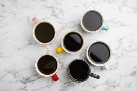 Many ceramic cups with hot aromatic coffee on marble background, flat lay