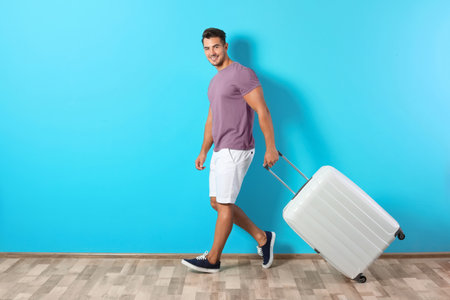 Young man walking with suitcase on color wall backgroundの写真素材