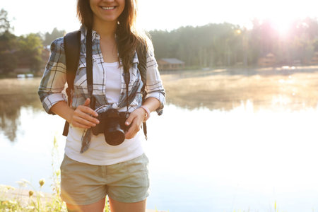 Young female photographer with camera near lake. Camping seasonの写真素材