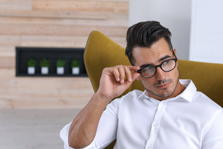 Portrait of handsome young man sitting in armchair indoors