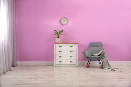 Stylish room interior with chest of drawers and rocking chair near color wallの写真素材