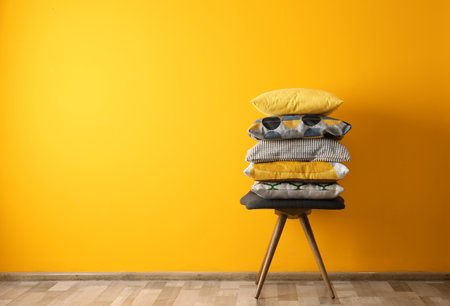 Many different pillows on chair near color wall with space for textの写真素材