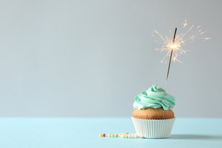 Delicious birthday cupcake with burning sparkler and space for text on light backgroundの写真素材