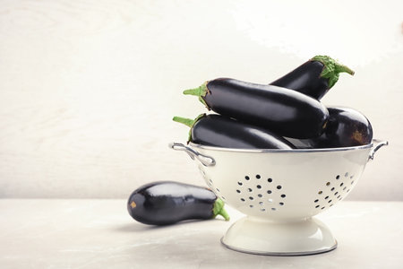 Colander with eggplants on table against light backgroundの写真素材
