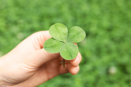 Woman holding four-leaf clover outdoors, closeupの写真素材