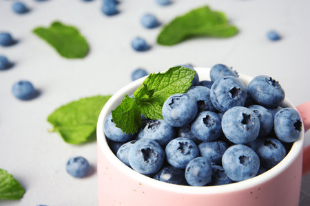 Cup with juicy blueberries and green leaves on color tableの写真素材