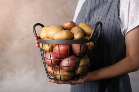 Person holding basket with fresh organic potatoes on color backgroundの写真素材