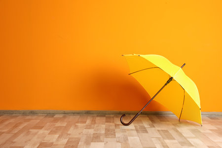 Beautiful open umbrella on floor near color wall with space for designの写真素材