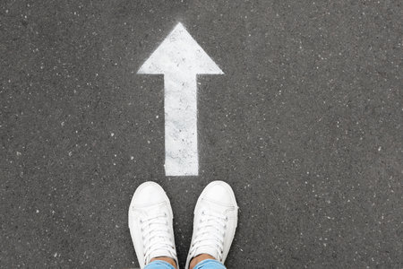 Woman standing near arrow on asphalt, top view. Choice conceptの写真素材