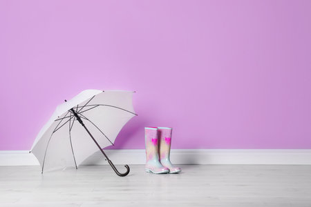 Beautiful open umbrella and gumboots on floor near color wall with space for designの写真素材