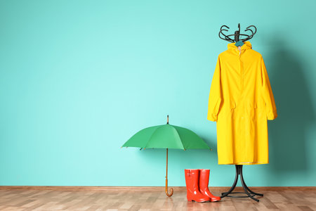 Umbrella, rain coat and boots near color wall with space for designの写真素材