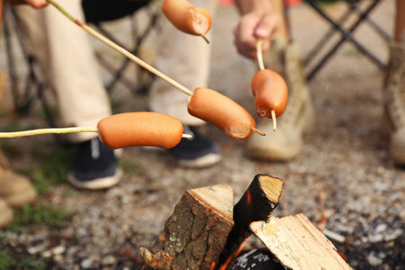 People frying sausages on bonfire outdoors. camping seasonの写真素材