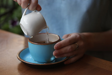 Woman adding water to fresh aromatic coffee at table, closeupの写真素材