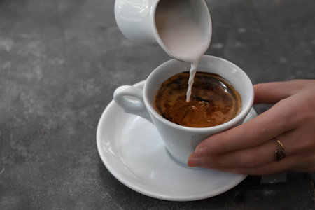 Woman adding milk to fresh aromatic coffee at table, closeup