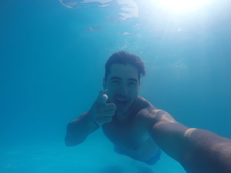 Handsome young man swimming in pool, underwater view