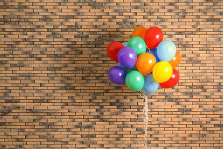 Bunch of bright balloons and space for text against brick wallの写真素材