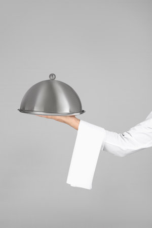 Waiter holding metal tray with lid on gray backgroundの写真素材