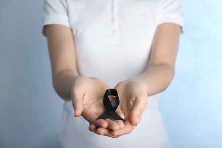 Woman holding black ribbon on light background, closeup. funeral symbolの写真素材