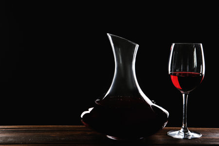 Elegant decanter and glass with red wine on table against dark backgroundの写真素材