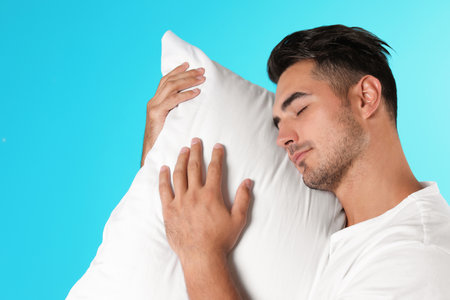 Young man with soft pillow on color backgroundの写真素材