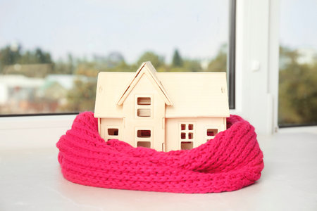 House model with knitted scarf on table against blurred background. heating conceptの写真素材