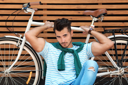 Handsome young hipster man with bicycle near wooden wall outdoors