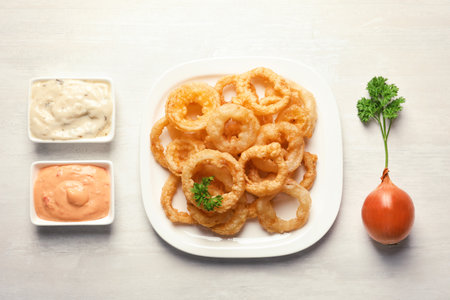 Plate with homemade crunchy fried onion rings and sauces on light background, top viewの写真素材