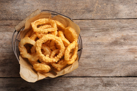 Homemade crunchy fried onion rings in wire basket on wooden background, top view. Space for textの写真素材