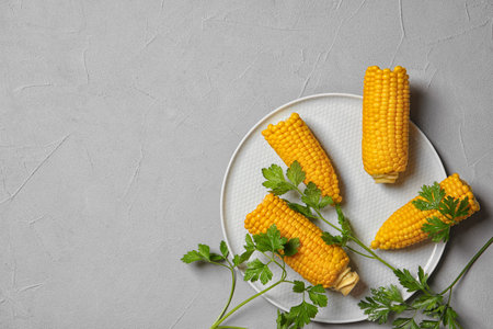 Plate with ripe corn cobs and parsley on gray background, top view. Space for text