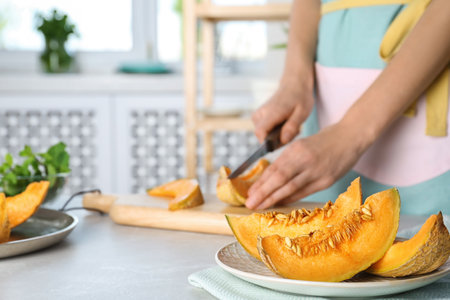 Woman slicing fresh ripe melon on light table
