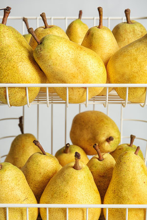Basket with fresh ripe pears on light background, closeup view