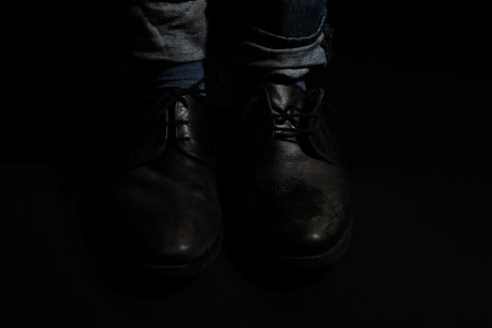 Poor man in dirty shoes on dark background, closeupの写真素材