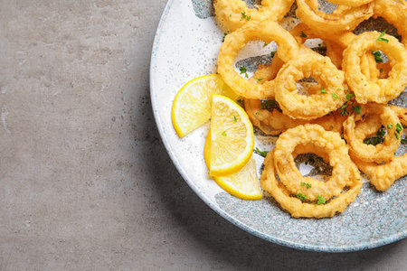 Plate with homemade crunchy fried onion rings and lemon slices on gray background, top view. Space for textの写真素材