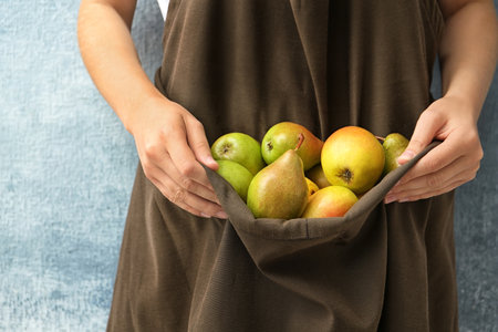 Woman in apron with ripe pears on color background, closeupの写真素材