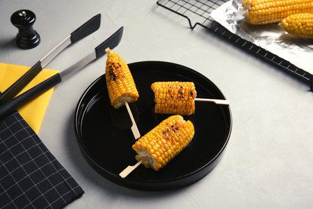 Ceramic plate with grilled corn cobs on light backgroundの写真素材
