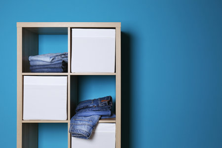 Stack of different jeans in wardrobe against color wall with space for textの写真素材