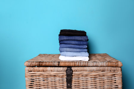 Stack of different jeans on basket against color wall
