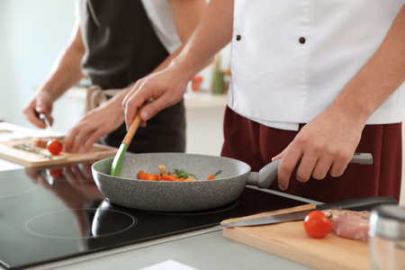 Male chef cooking vegetables on electric stove, closeupの写真素材