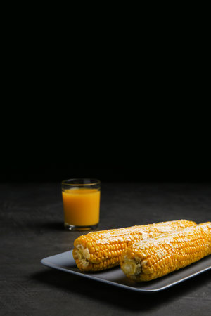 Delicious boiled corn cobs with butter on gray table against black background. Space for textの写真素材