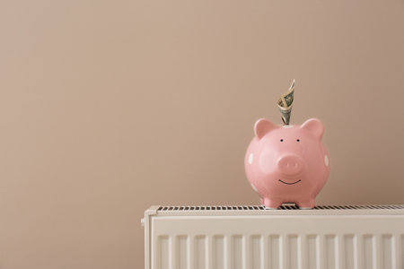 Heating radiator with piggy bank and money near color wall. Space for textの写真素材