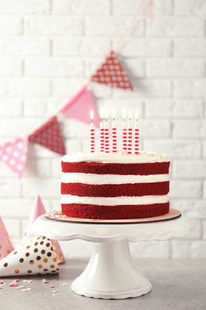 Delicious homemade red velvet cake with candles on table against brick wallの写真素材
